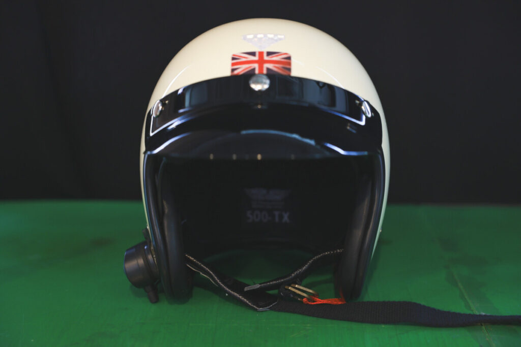 Front-facing view of the ivory slim-shell motorcycle helmet sitting on a green surface, emphasizing its compact shape