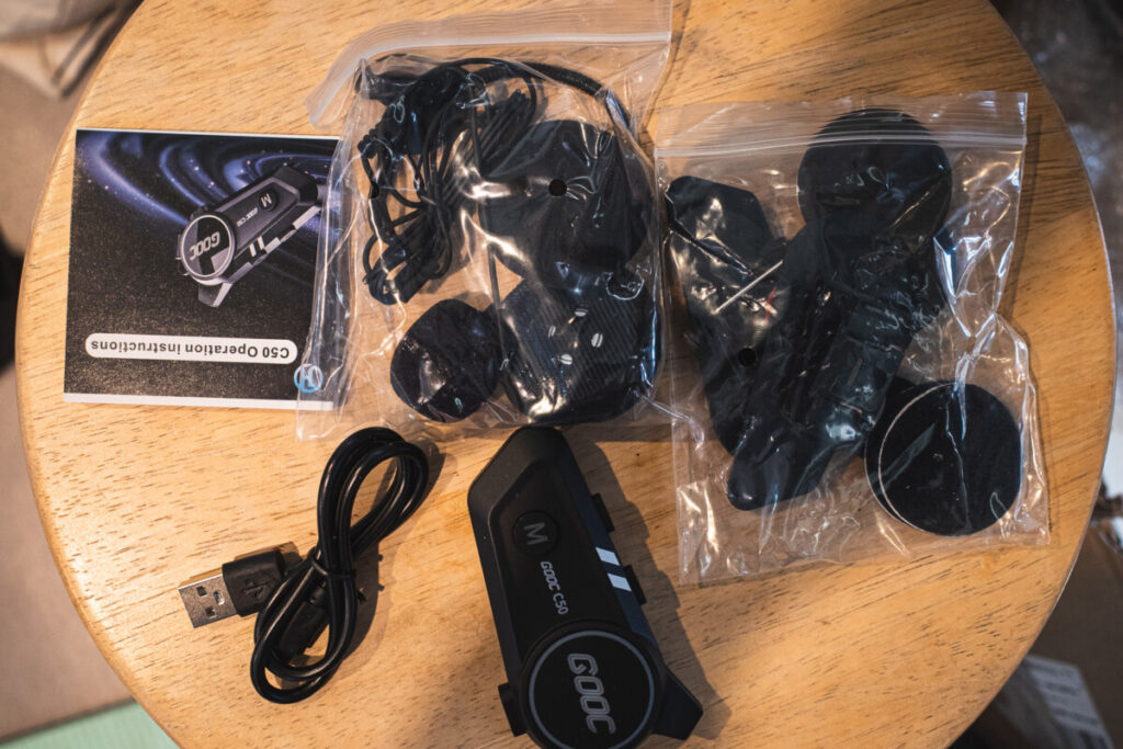 "GOOC C50 Bluetooth headset full package laid out on a wooden table, including the main device, USB charging cable, mounting accessories, speakers, microphone, and instruction manual."