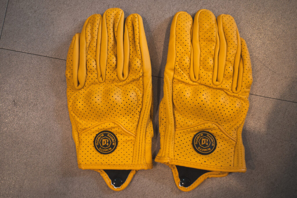 A pair of yellow perforated leather motorcycle gloves with hard knuckle protection, laid flat side by side on a gray surface.