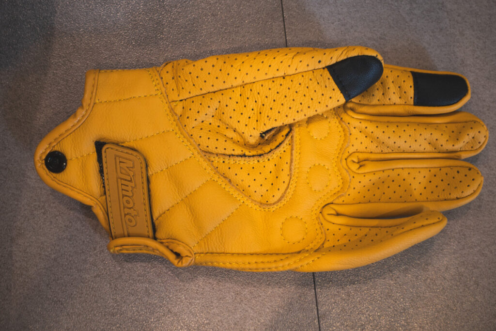 Top-down view of a yellow mymoto motorcycle glove showing the palm side, touchscreen fingertips, and wrist strap.