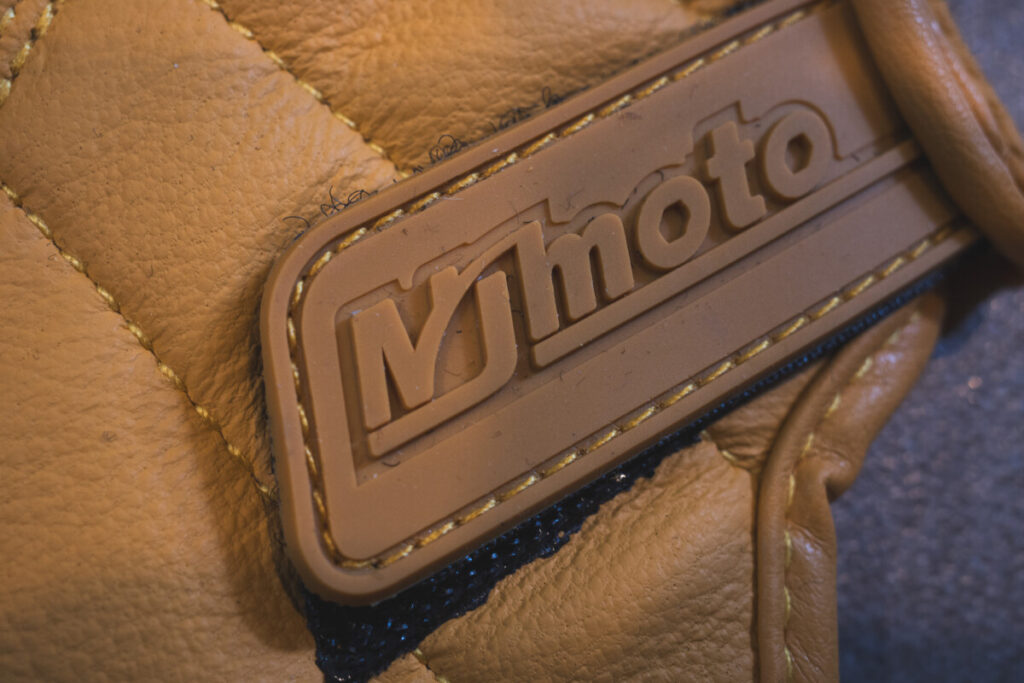 Macro shot of the stitched mymoto brand logo on a yellow motorcycle glove.