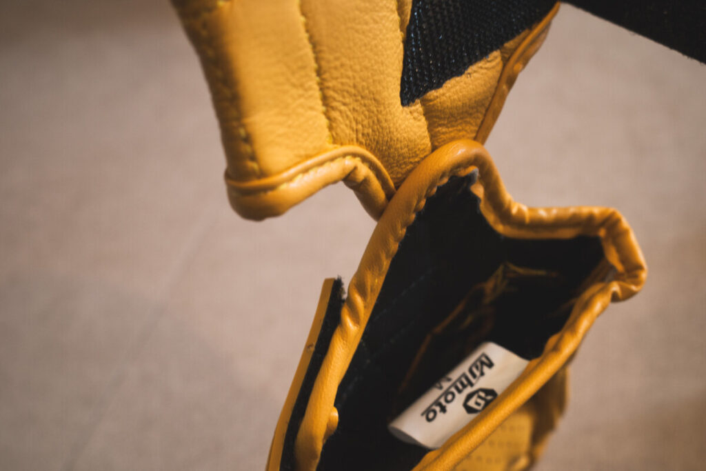 Zoomed-in view of the inner finger seam and stitching on a yellow leather motorcycle glove.
