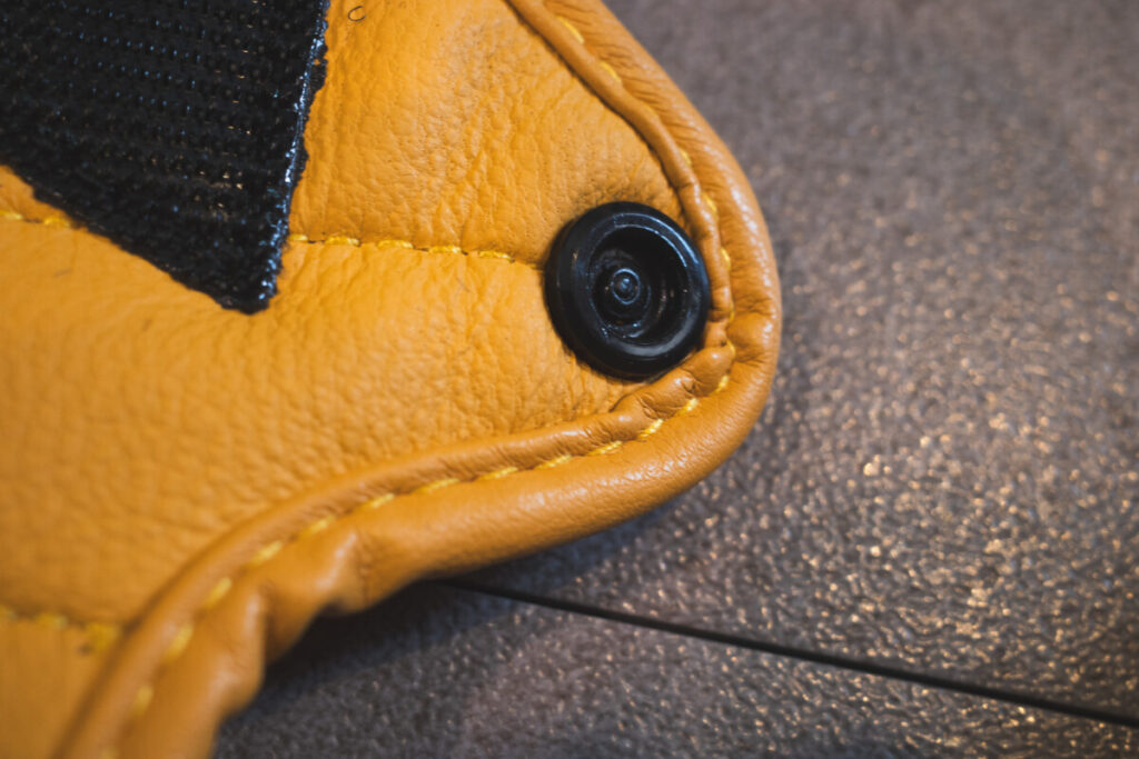 Close-up of the snap button on the wrist of a yellow leather motorcycle glove.