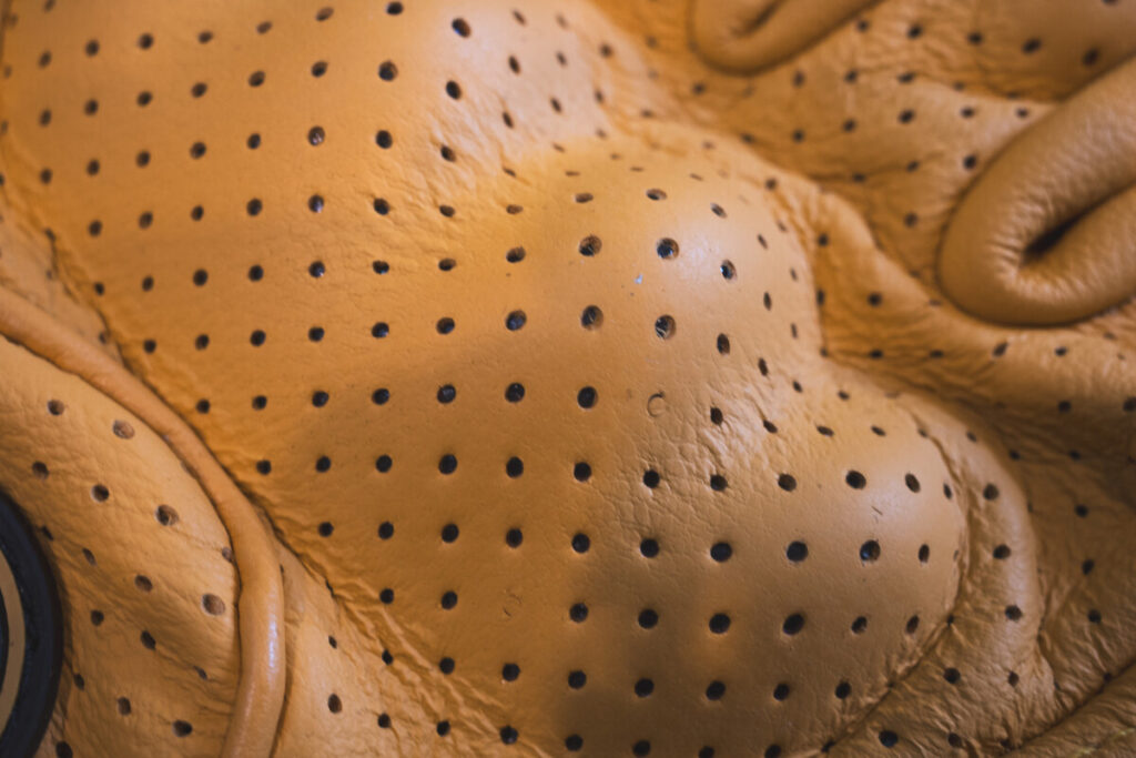 Detailed view of the perforated knuckle area on a yellow ventilated motorcycle glove.