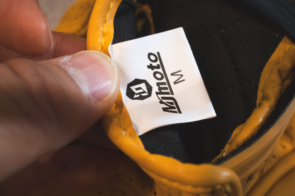 Close-up of a hand holding the inner label of a mymoto motorcycle glove, showing size M.