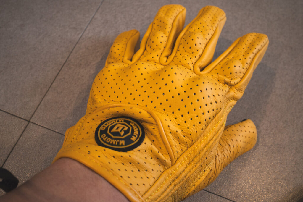 Wearing a yellow ventilated motorcycle glove with visible perforations and a protective knuckle shell.