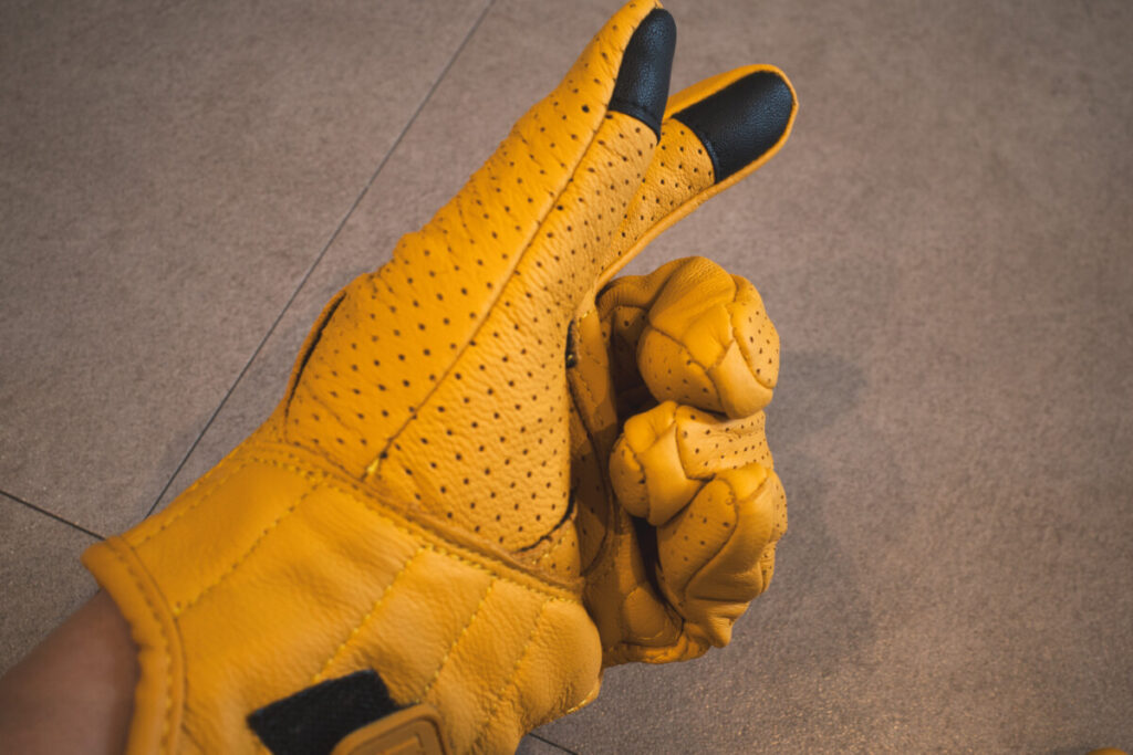 Side view of a gloved hand in a partially closed fist, showing black touchscreen fingertips on the thumb and index finger.