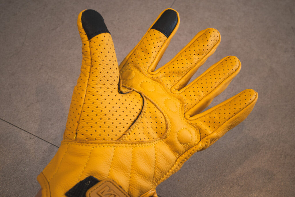 Palm-side view of a yellow motorcycle glove with ventilation holes and black touchscreen-compatible tips.