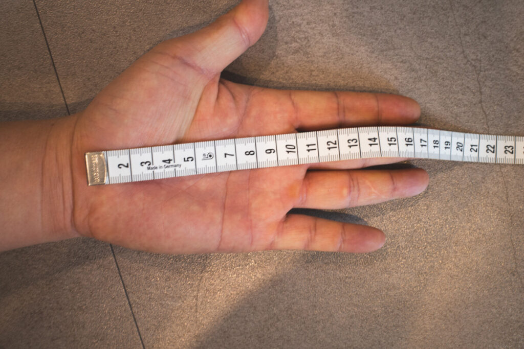Hand laid flat with a measuring tape across the palm, measuring total hand width.