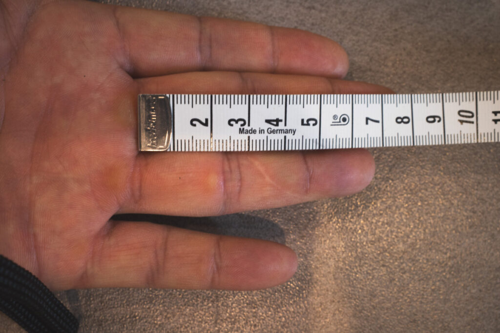 Palm of a hand being measured horizontally across the widest part with a tape measure.