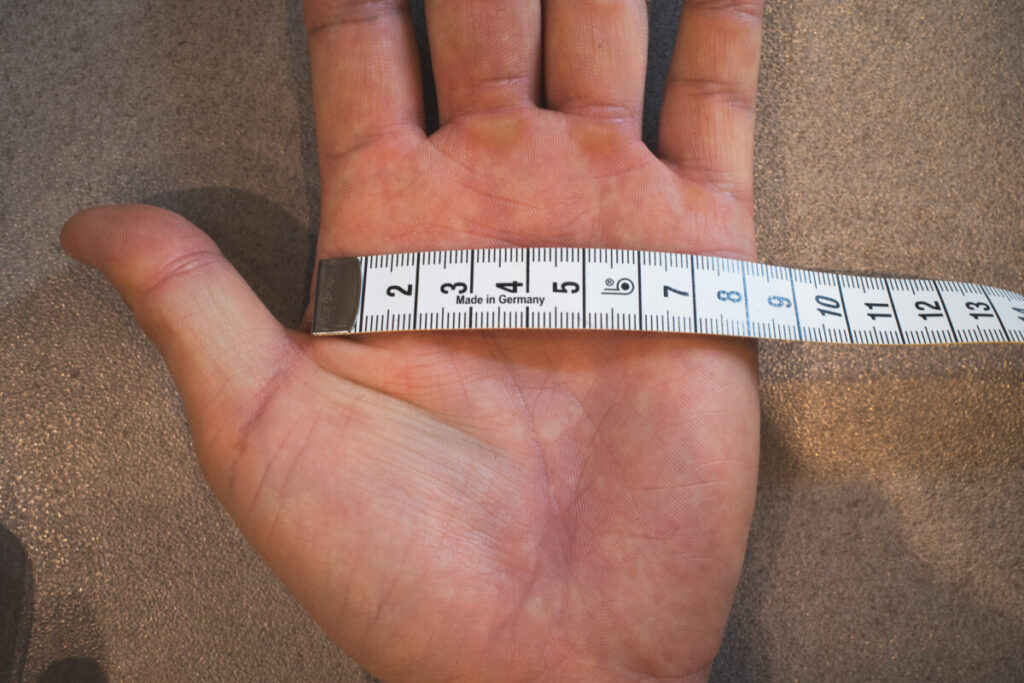 Measuring tape wrapped around the palm to measure hand circumference for glove sizing.