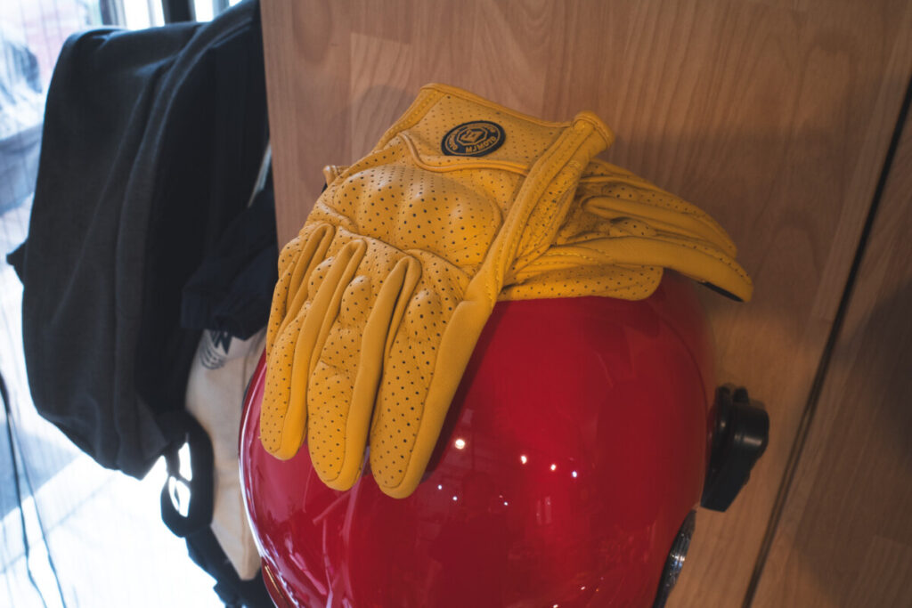 A pair of yellow ventilated motorcycle gloves neatly placed on top of a glossy red helmet indoors.