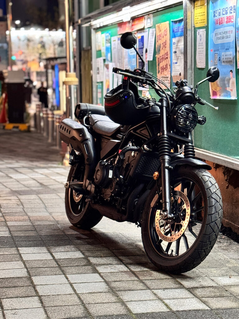 Honda CL500 parked in a Seoul alley at night with a helmet on the handlebar