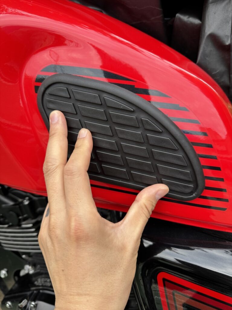 Checking the knee position of a black rubber side tank pad on a red Keeway SR125 fuel tank