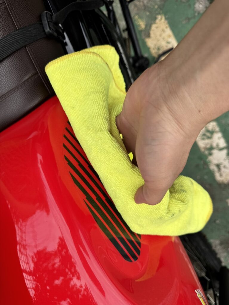 Cleaning the red motorcycle fuel tank with a microfiber towel before applying a side tank pad