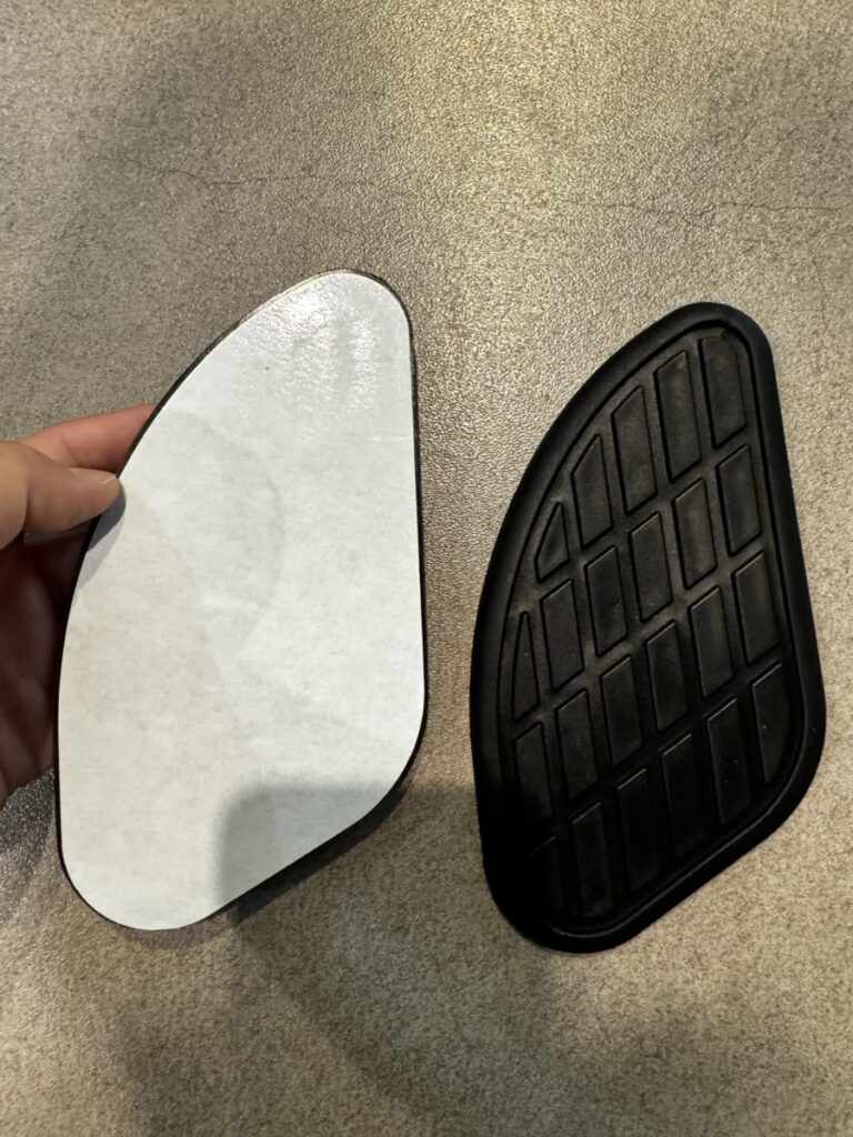 Front and adhesive side of a black rubber motorcycle side tank pad before installation