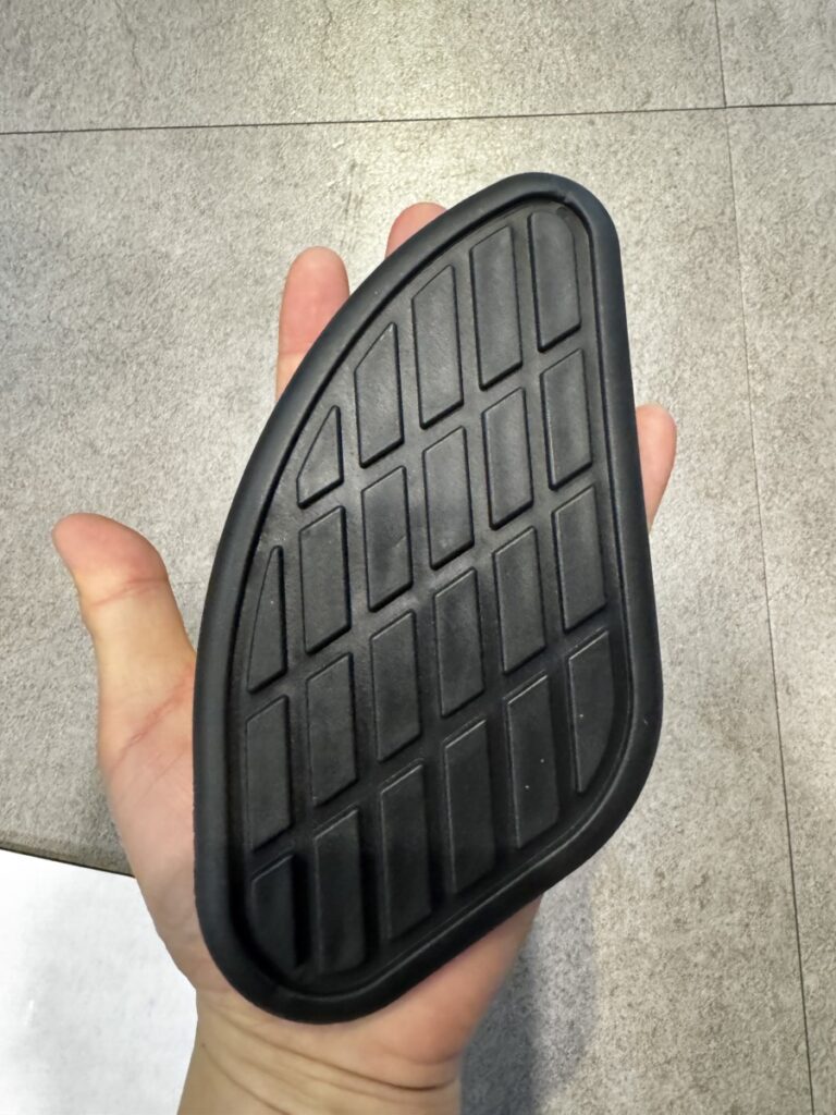 Hand holding a palm-sized black rubber motorcycle tank grip pad with vintage grid pattern