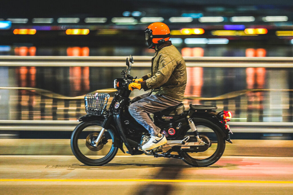 Rider on a Honda Super Cub 110 crossing a Han River bridge at night in Seoul
